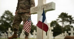 Why Americans Still Cross the Atlantic for Omaha Beach: Inside Normandy’s Most Powerful Journey French and American flags beside a white cross at Normandy American Cemetery