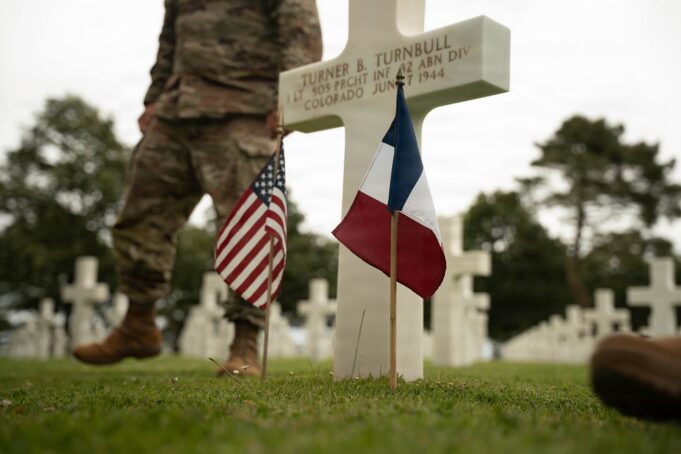 French and American flags beside a white cross at Normandy American Cemetery