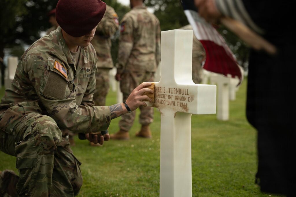 US soldier respectfully cleaning a white grave cross at Normandy American Cemetery