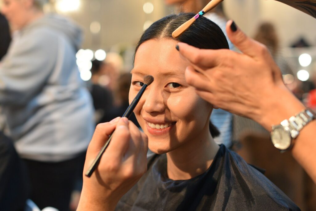 Liu Wen smiling during makeup preparation backstage at a Prada fashion show