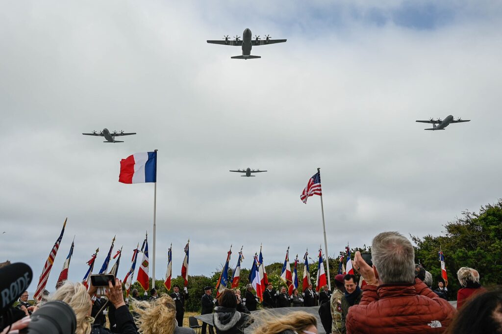 French and American flags beneath a commemorative flyover at Pointe du Hoc in Normandy