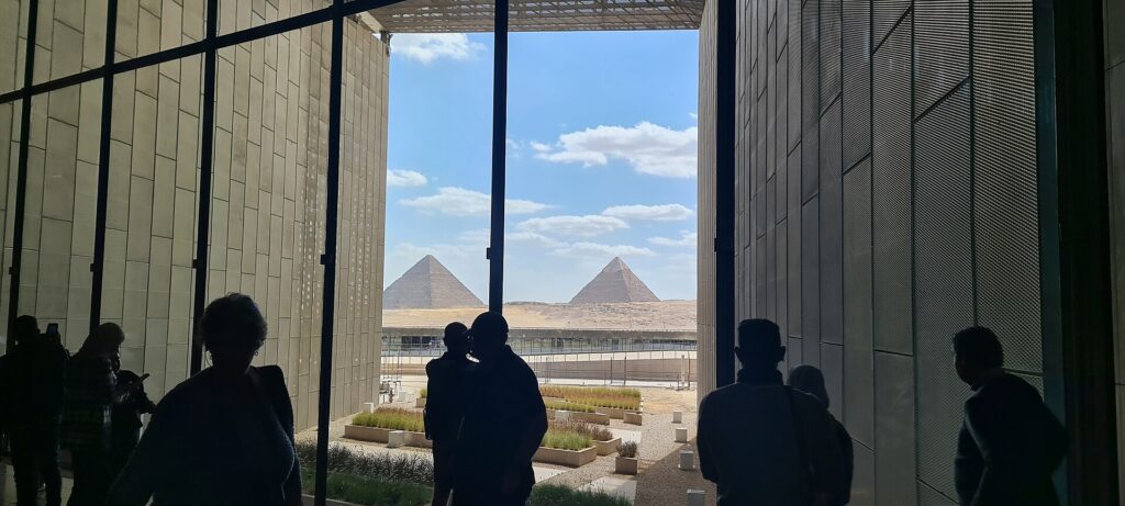 Visitors looking toward the Giza Pyramids through the Grand Egyptian Museum architecture