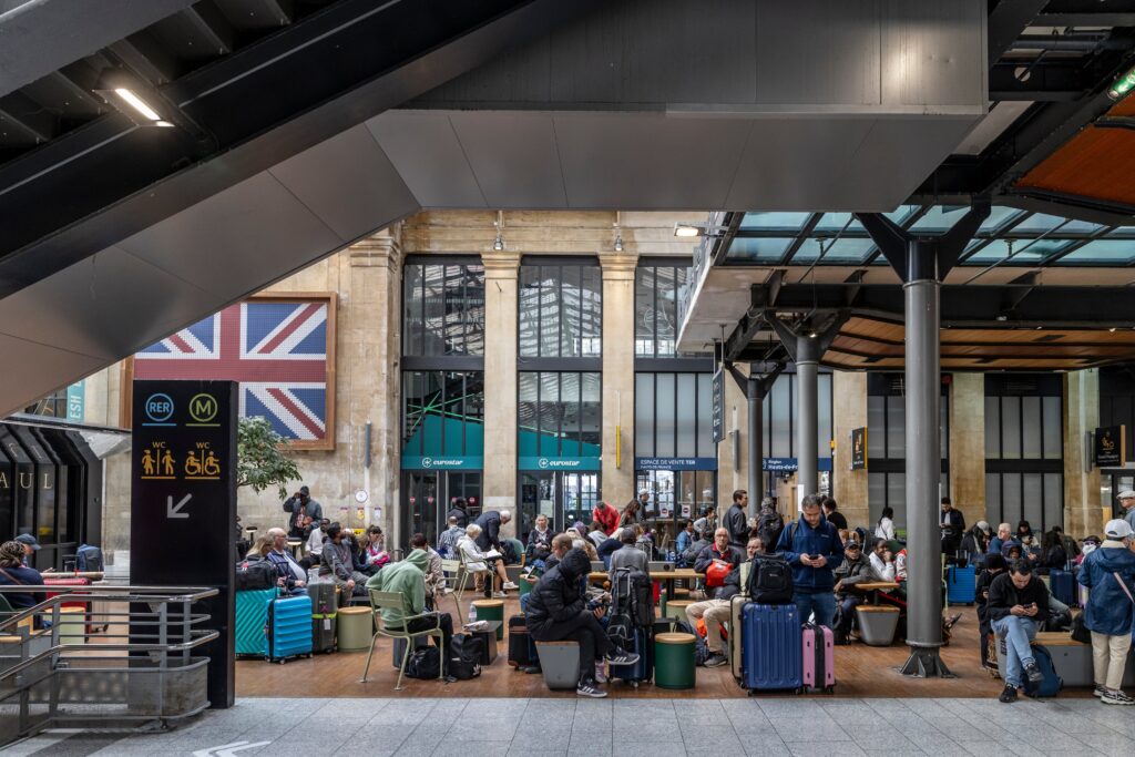 Eurostar passengers waiting with suitcases beneath a United Kingdom sign inside Paris Gare du Nord