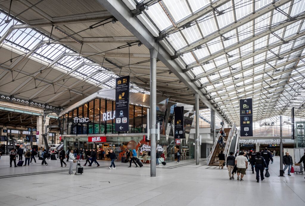 Travellers crossing the bright renovated concourse inside Paris Gare du Nord with directional signs overhead