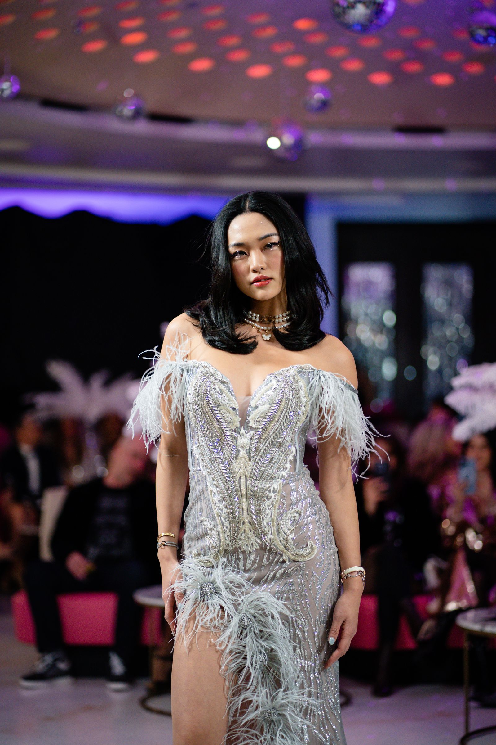 Glamorous fashion model in an elegant feathered dress walking a runway before an audience