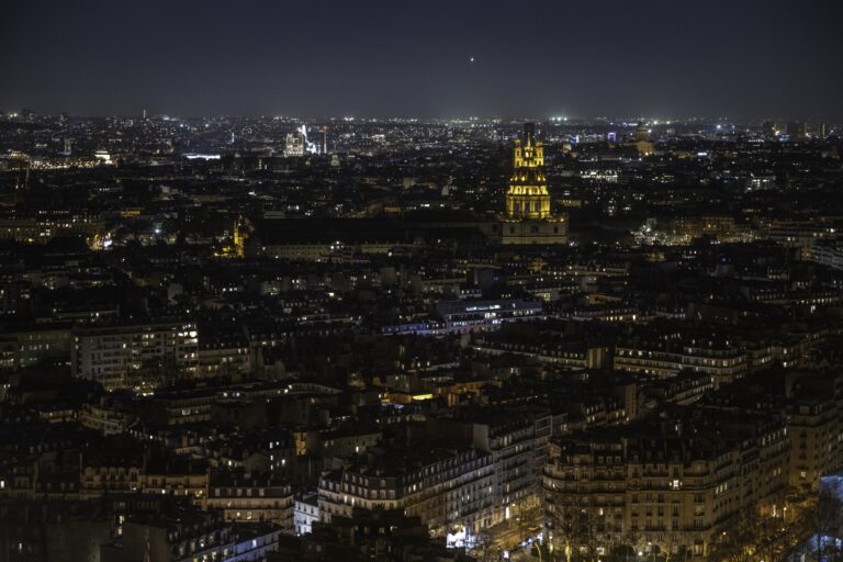 Night panorama across Paris neighborhoods from the Eiffel Tower, with Les Invalides illuminated