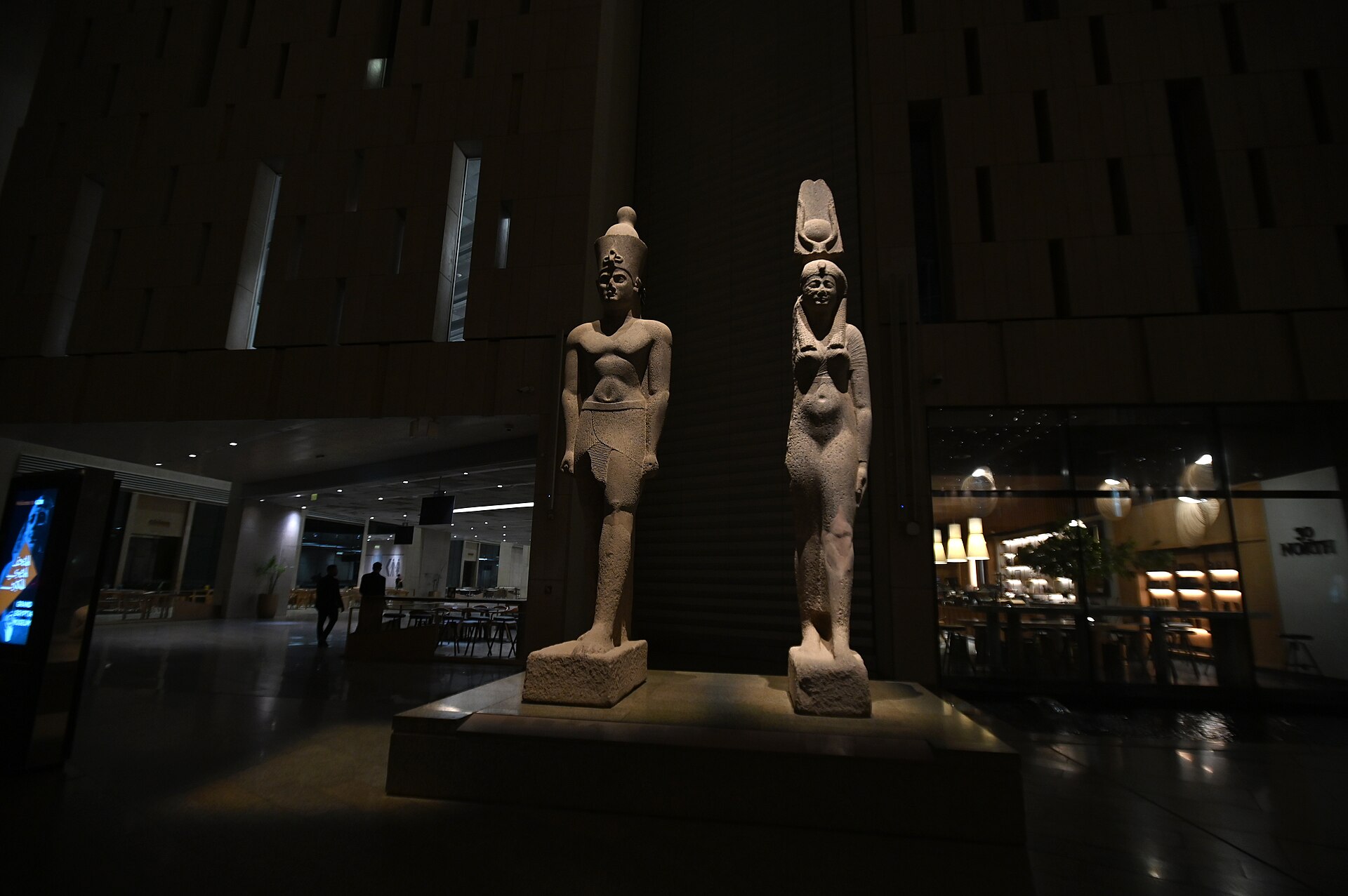 Two ancient Egyptian sculptures illuminated inside the Grand Egyptian Museum at night
