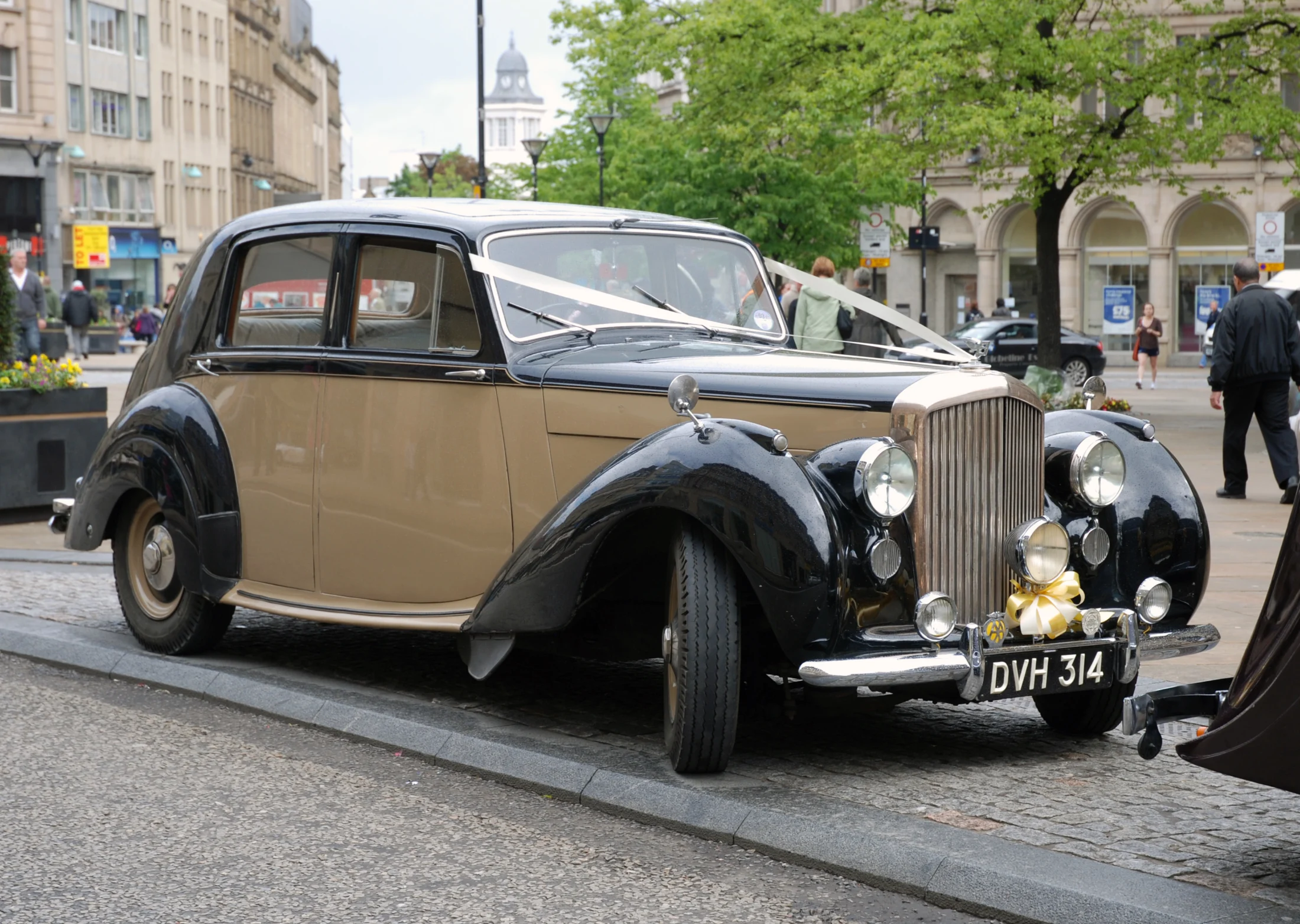 Ribbon-decorated Bentley wedding car outside a town hall