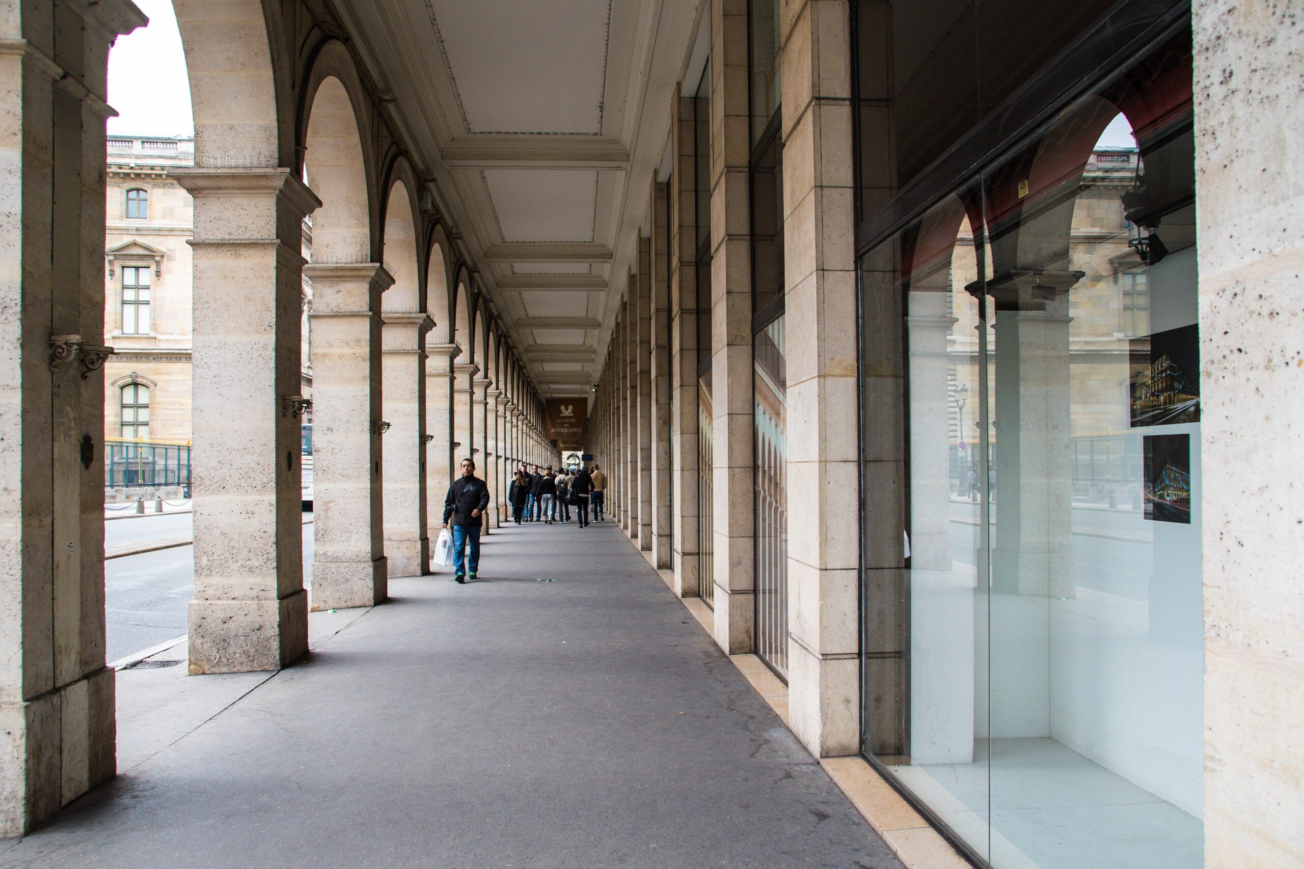 Long covered shopping arcade on Rue de Rivoli with pedestrians and reflective shop windows