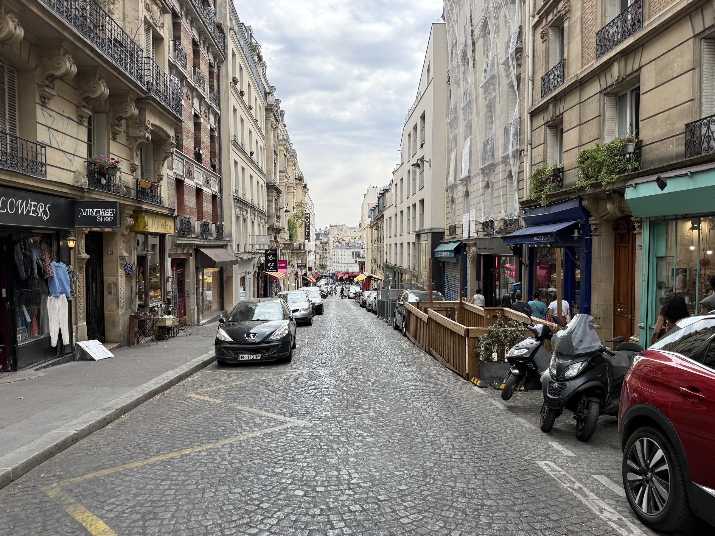 Cobbled upper Rue des Martyrs lined with cafés shops and pedestrians in Paris’s 18th arrondissement in July 2026