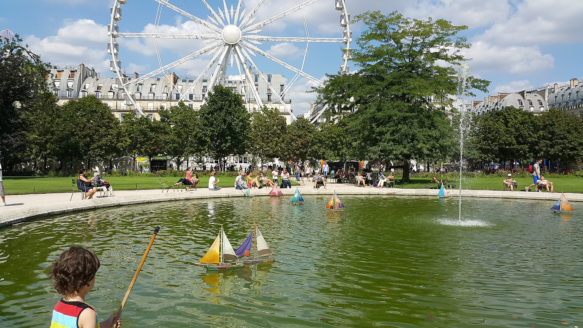 Child sailing a small toy boat on the pond in the Tuileries Garden in Paris