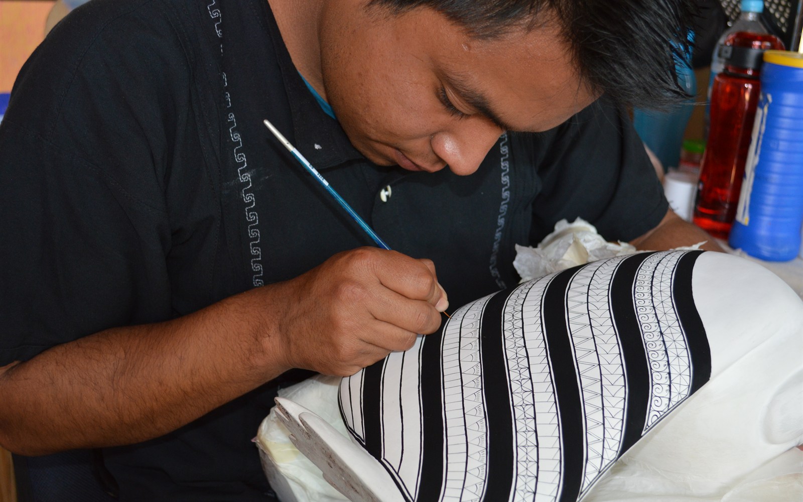 Un jeune artisan peint les détails d’un alebrije à San Martín Tilcajete : visage, main et créature replacent l’auteur humain au centre de l’image.