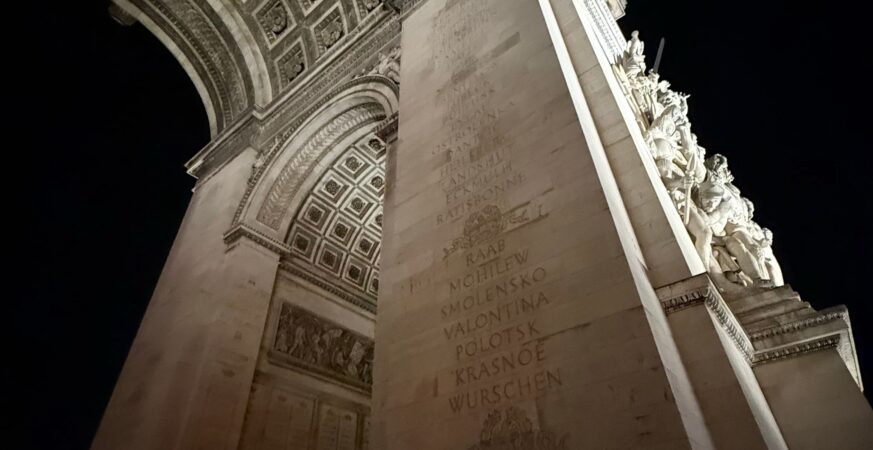 Architectural details beneath the Arc de Triomphe illuminated at night in Paris