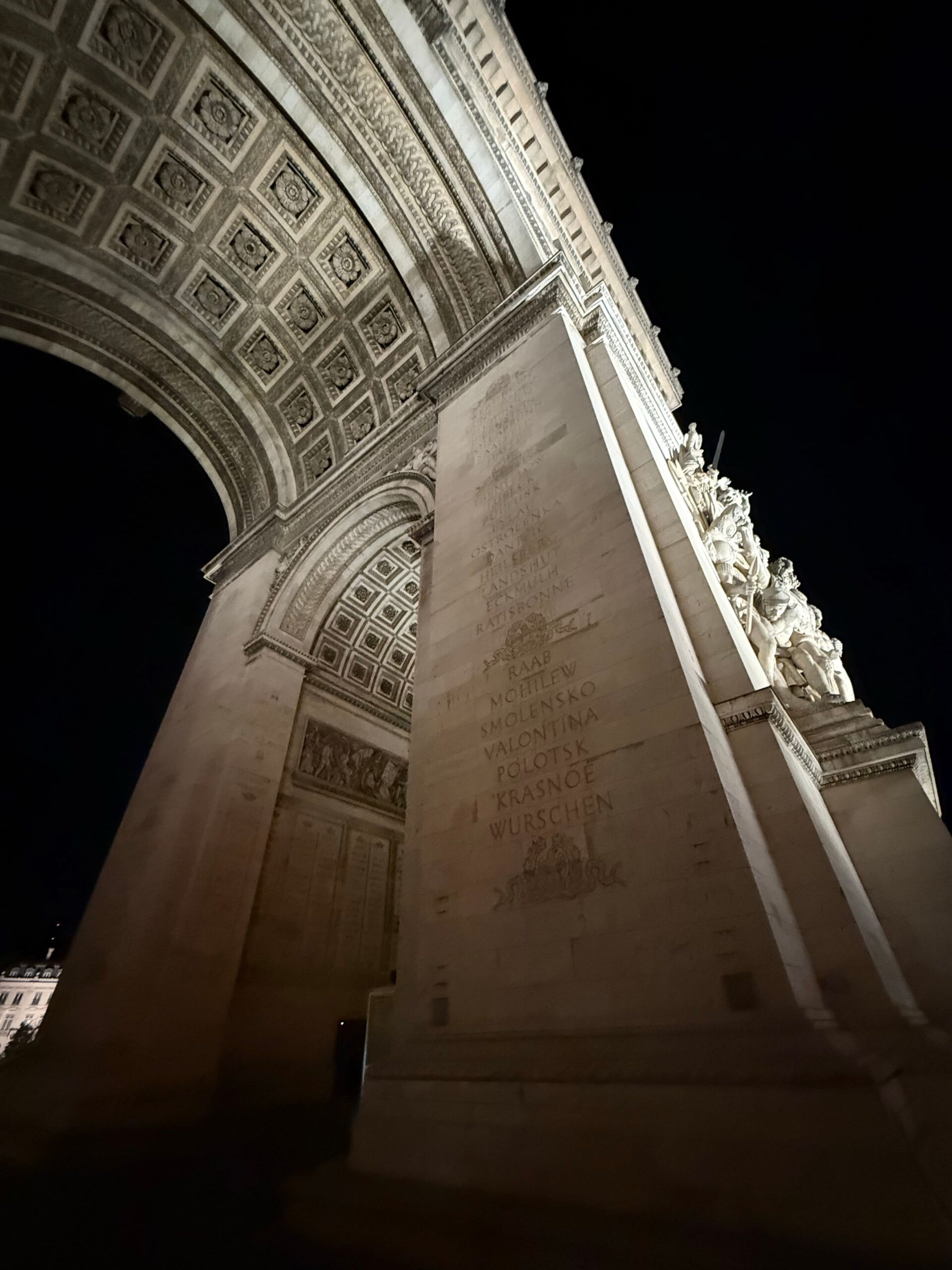 Architectural details beneath the Arc de Triomphe illuminated at night in Paris