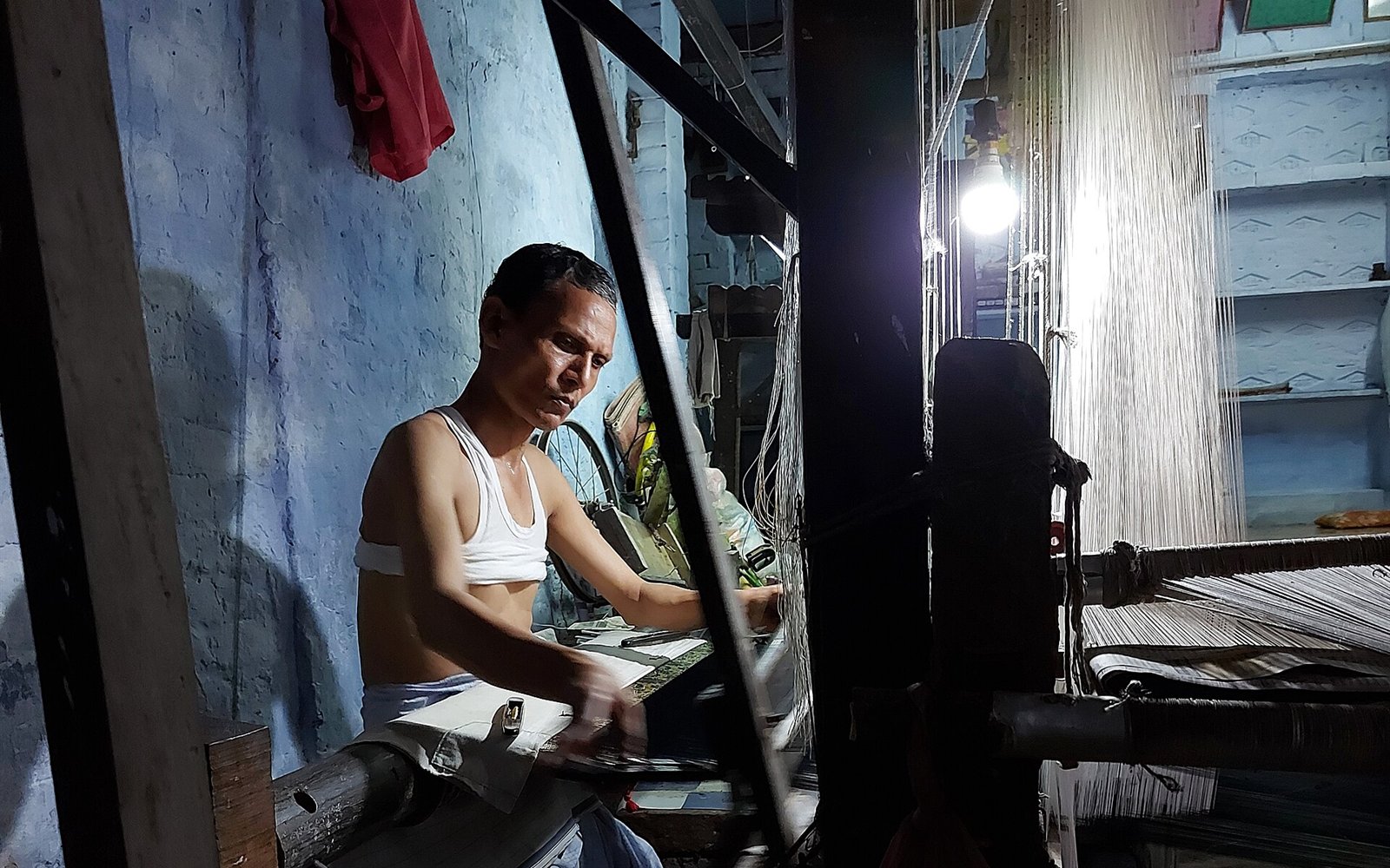 A handloom weaver in Varanasi: face, moving hand and illuminated warp show that luxury begins in the workroom, not the shop window.