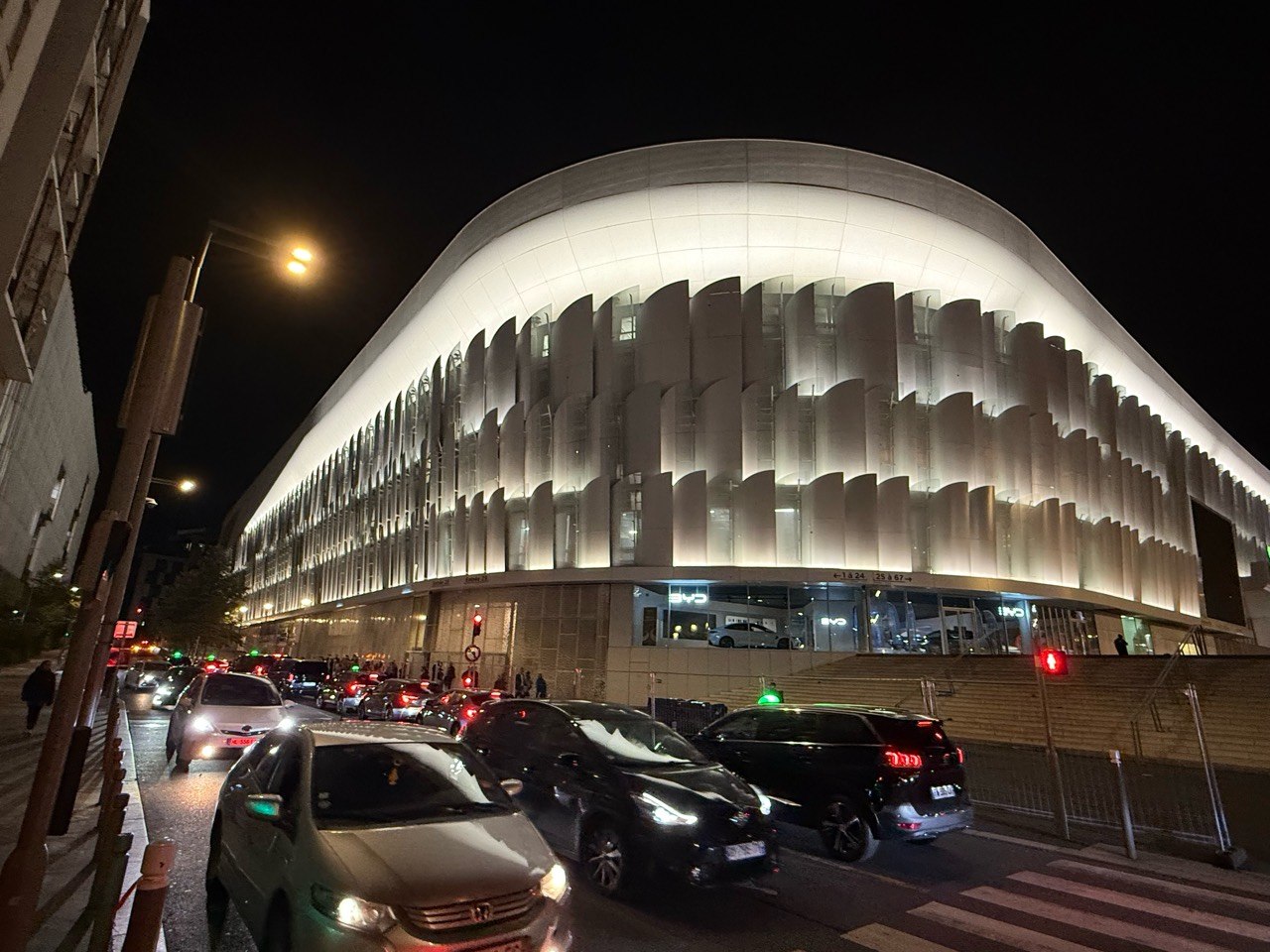 Late-night traffic beside the illuminated Plenitude Arena after the concert