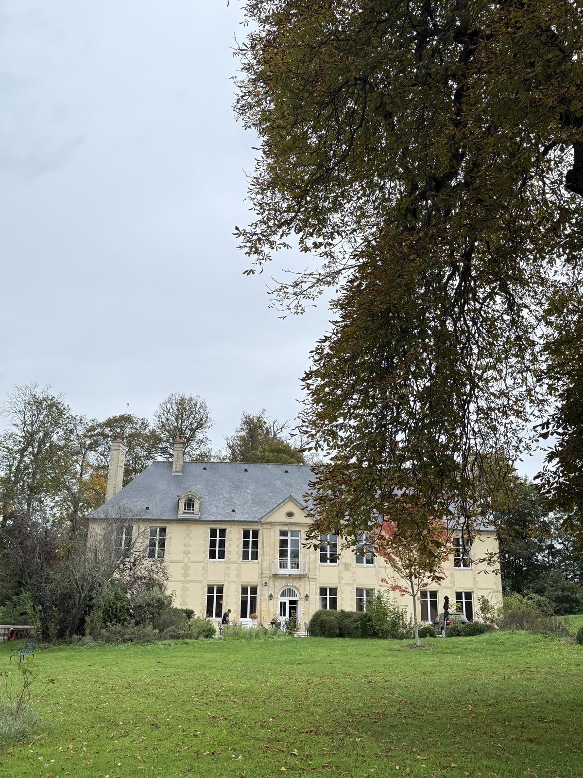 Full façade of Château de Bellefontaine framed by a mature tree and lawn