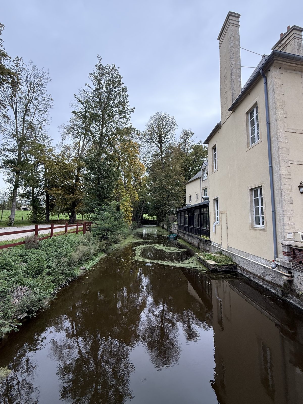 Reflective water and trees beside Château de Bellefontaine in Bayeux