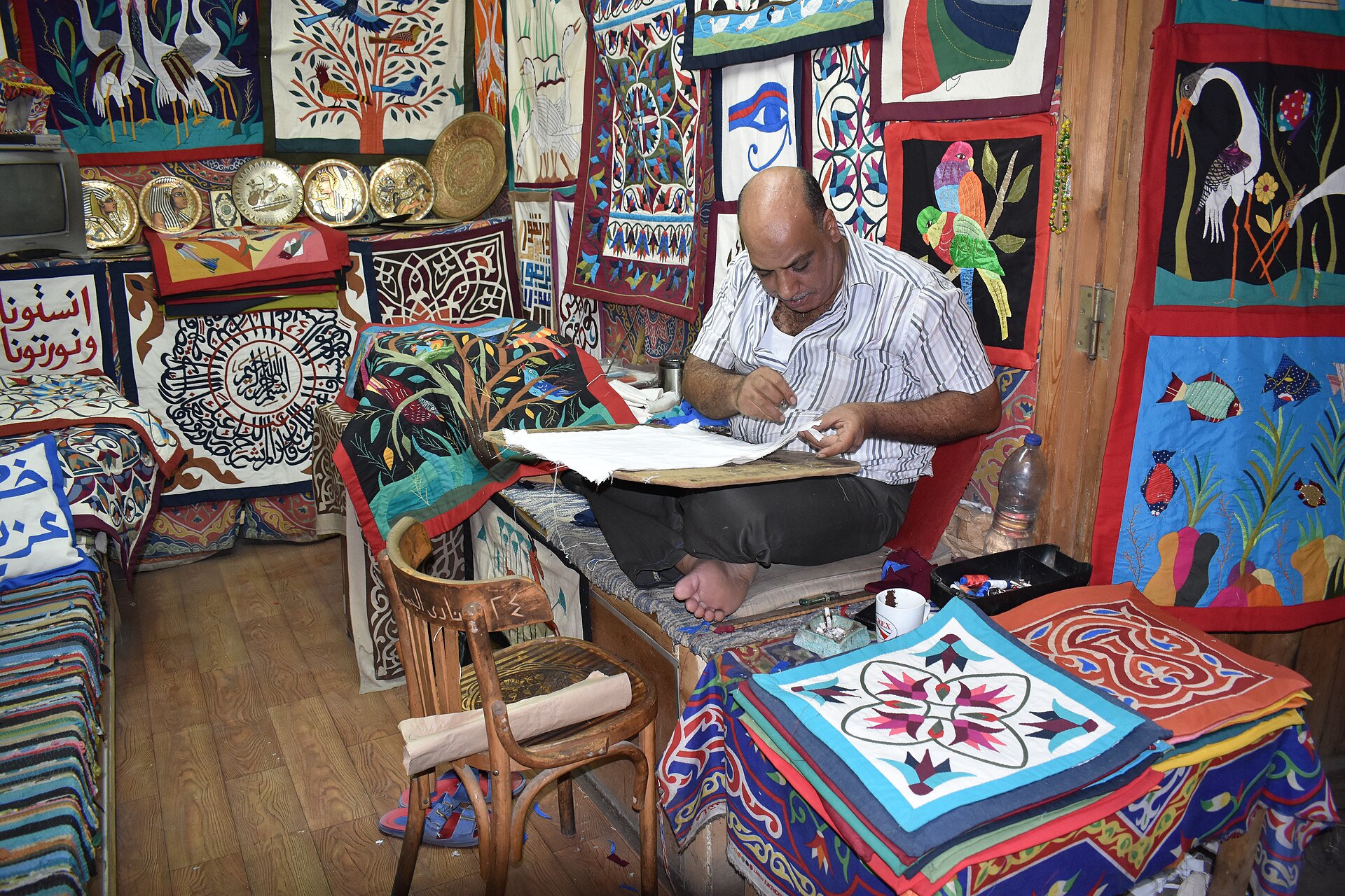 A khayamiya artisan stitches inside his workshop on Cairo’s Street of the Tentmakers; face, hand and cloth share the frame.