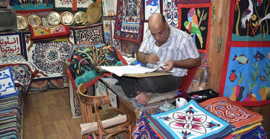 Un artisan de la khayamiya coud dans son atelier de la rue des fabricants de tentes au Caire ; visage, main et étoffe partagent l’image.