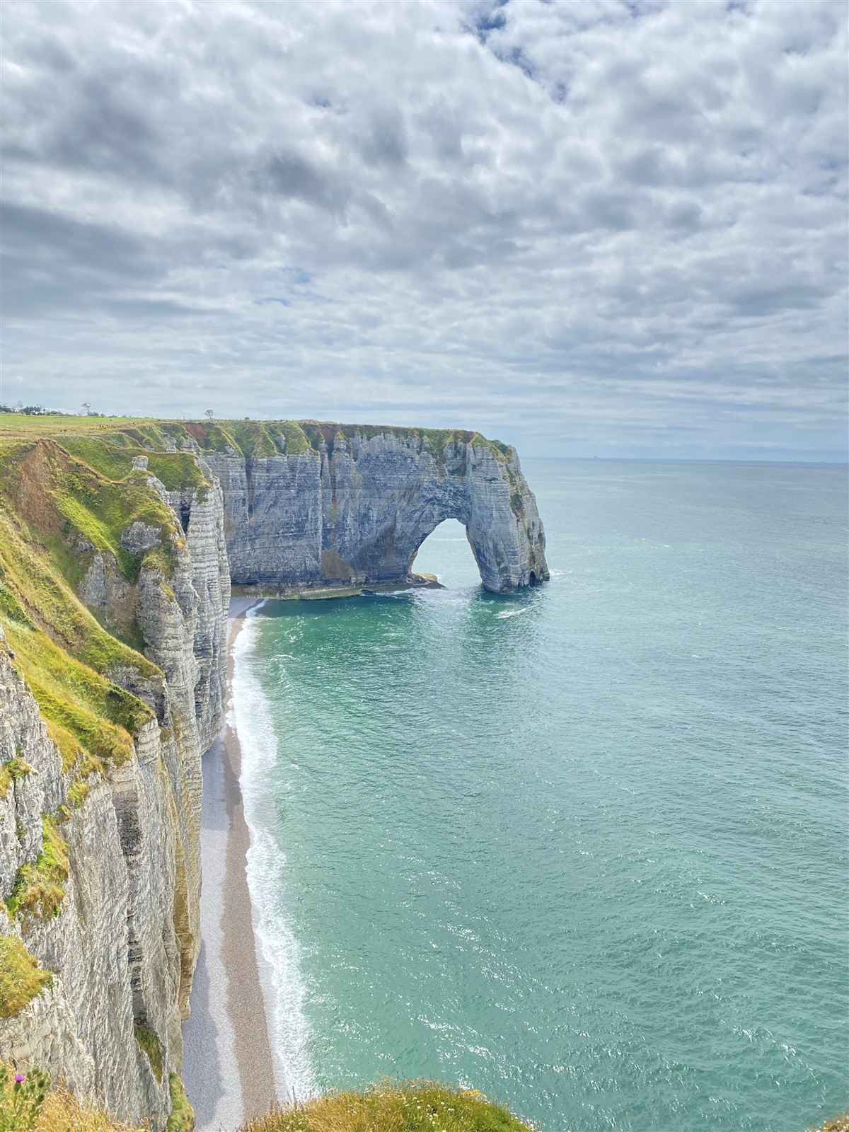 A chalk arch and ribbon of beach seen from higher ground in Étretat.