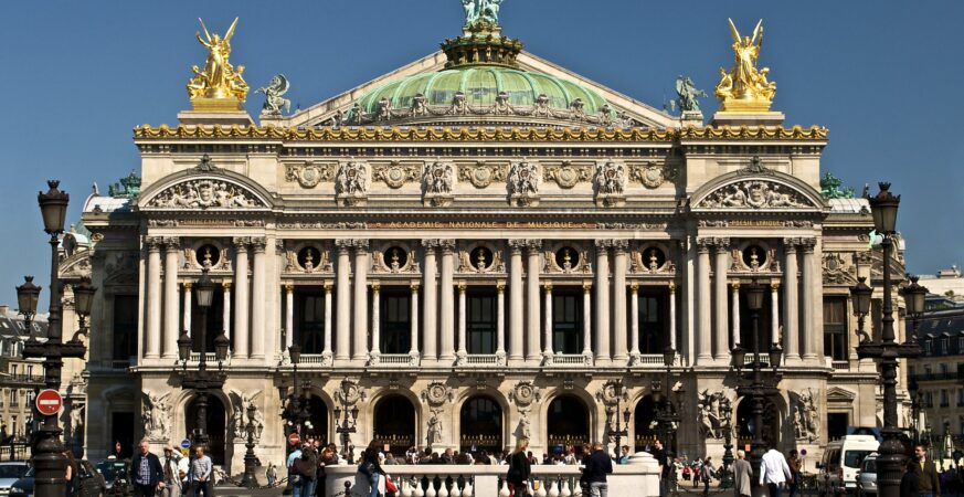 Bright frontal view of the Palais Garnier façade in Paris with incidental pedestrians on Place de l’Opéra