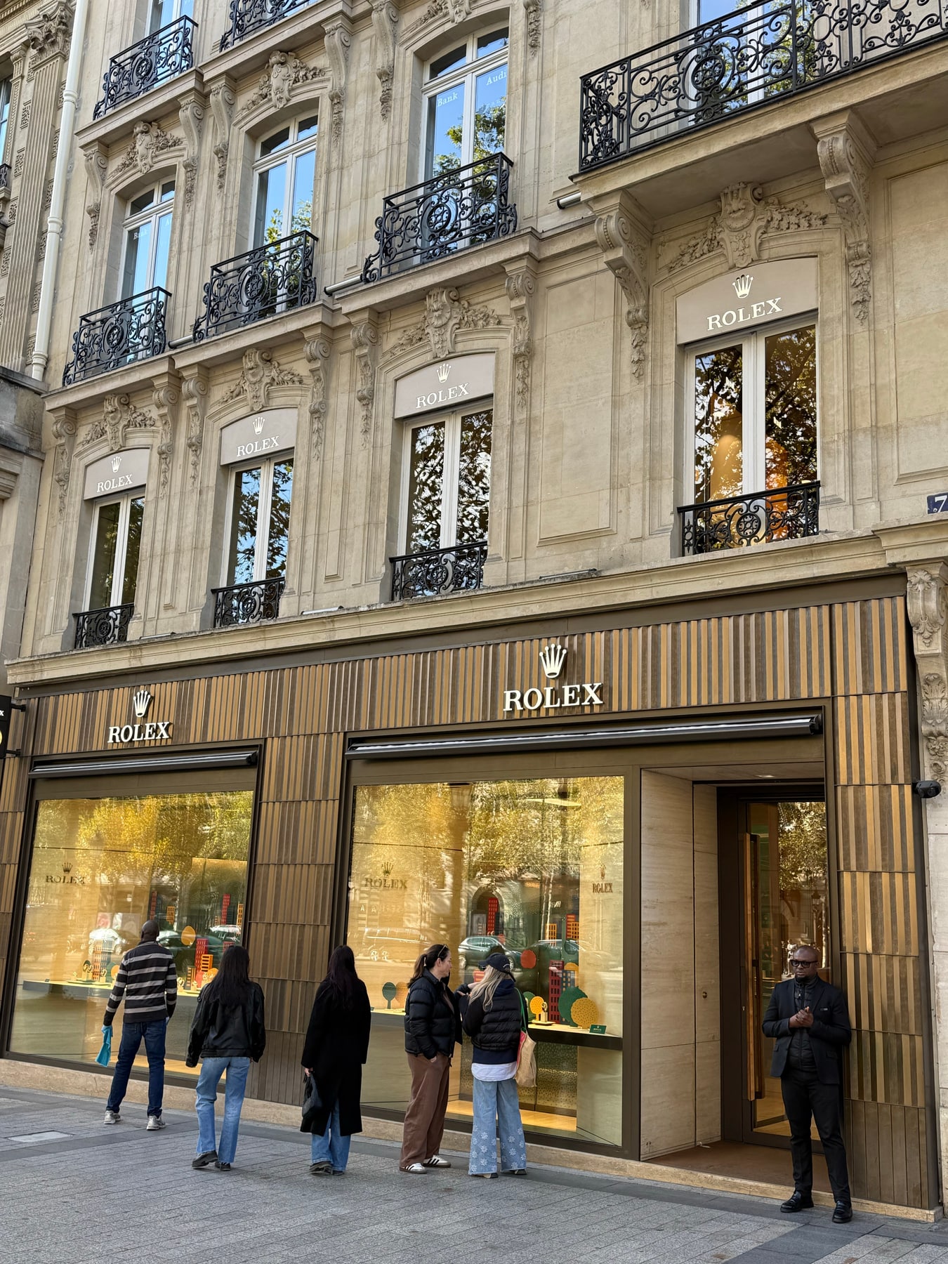 Visiteurs et agent de sécurité devant la boutique Rolex ouverte sur les Champs-Élysées dimanche matin