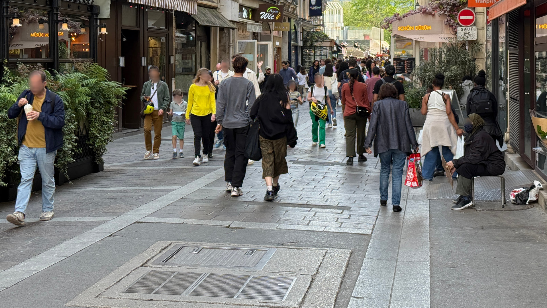 Pedestrians walking past cafés, food shops and flower displays on Rue Montorgueil in Paris.
