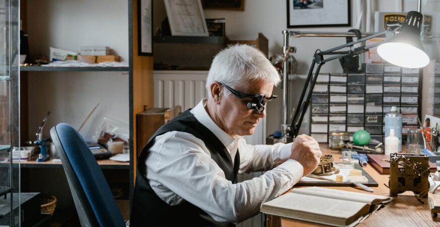 A watchmaker at the bench: face, loupe, hand and mechanism in one frame, placing the human being inside the story of precision. The photograph illustrates the craft rather than a named Swiss workshop.