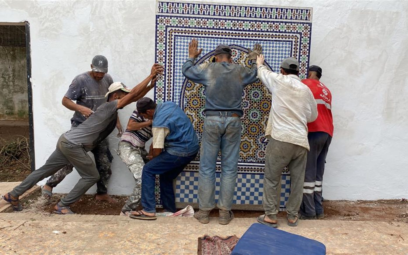 Artisans position a large mosaic fountain, showing the collective labour behind a finished zellige work.